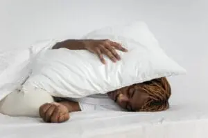 https://www.pexels.com/photo/man-sleeping-with-pillow-on-his-head-7445324/ African American man sleeping with a pillow over his head